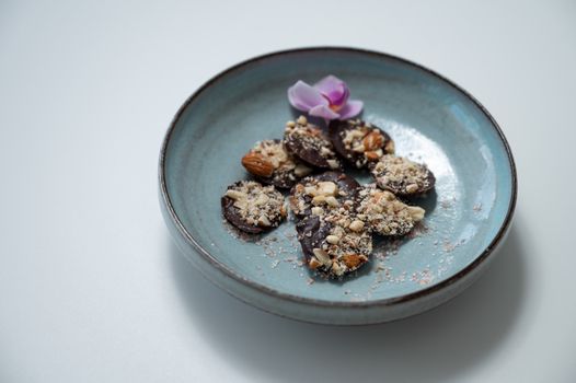Delicious chocolate bark sprinkled with nuts, served in a ceramic bowl with an orchid garnish.