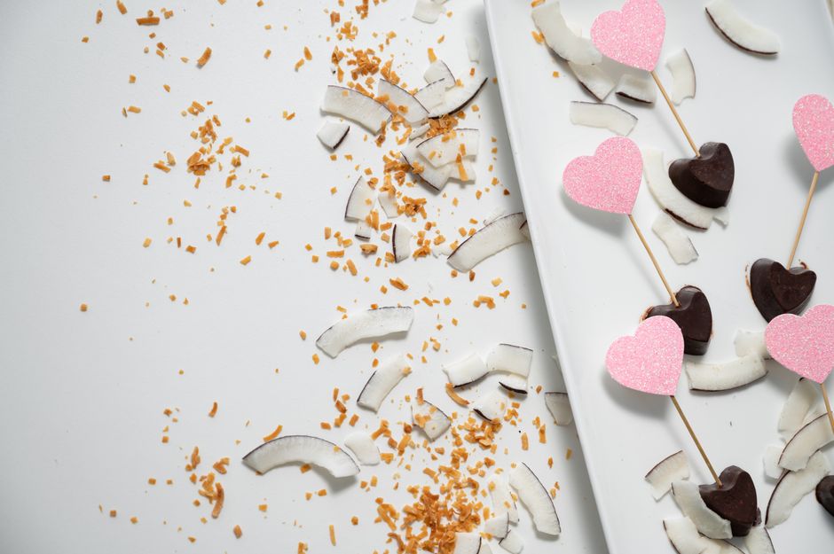 Artistic flat lay of heart-shaped chocolates and coconut slices, perfect for Valentine's Day.