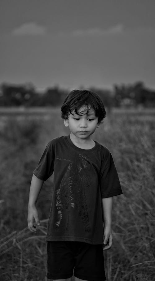 Grayscale Photo of a Boy Standing on a Grassy Field