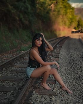 Stylish woman in black top and shorts sitting on railway tracks outdoors.