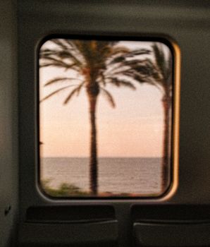 Blurred view of palm trees and sea from a train window in Santa Susanna, Spain.