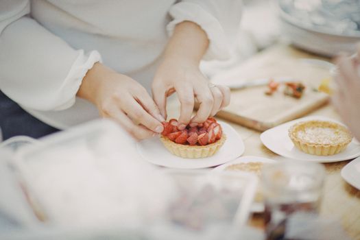 Hands setting strawberries on homemade tarts, showcasing food preparation with fresh ingredients.