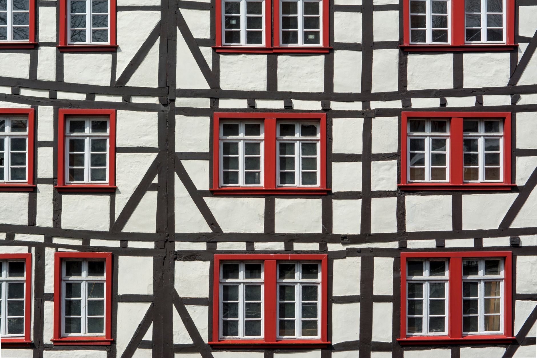 Detailed view of a half-timbered building facade featuring red window frames and geometric patterns.