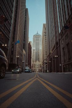 Low angle view of a city street lined with skyscrapers and parked cars, captured at dusk.