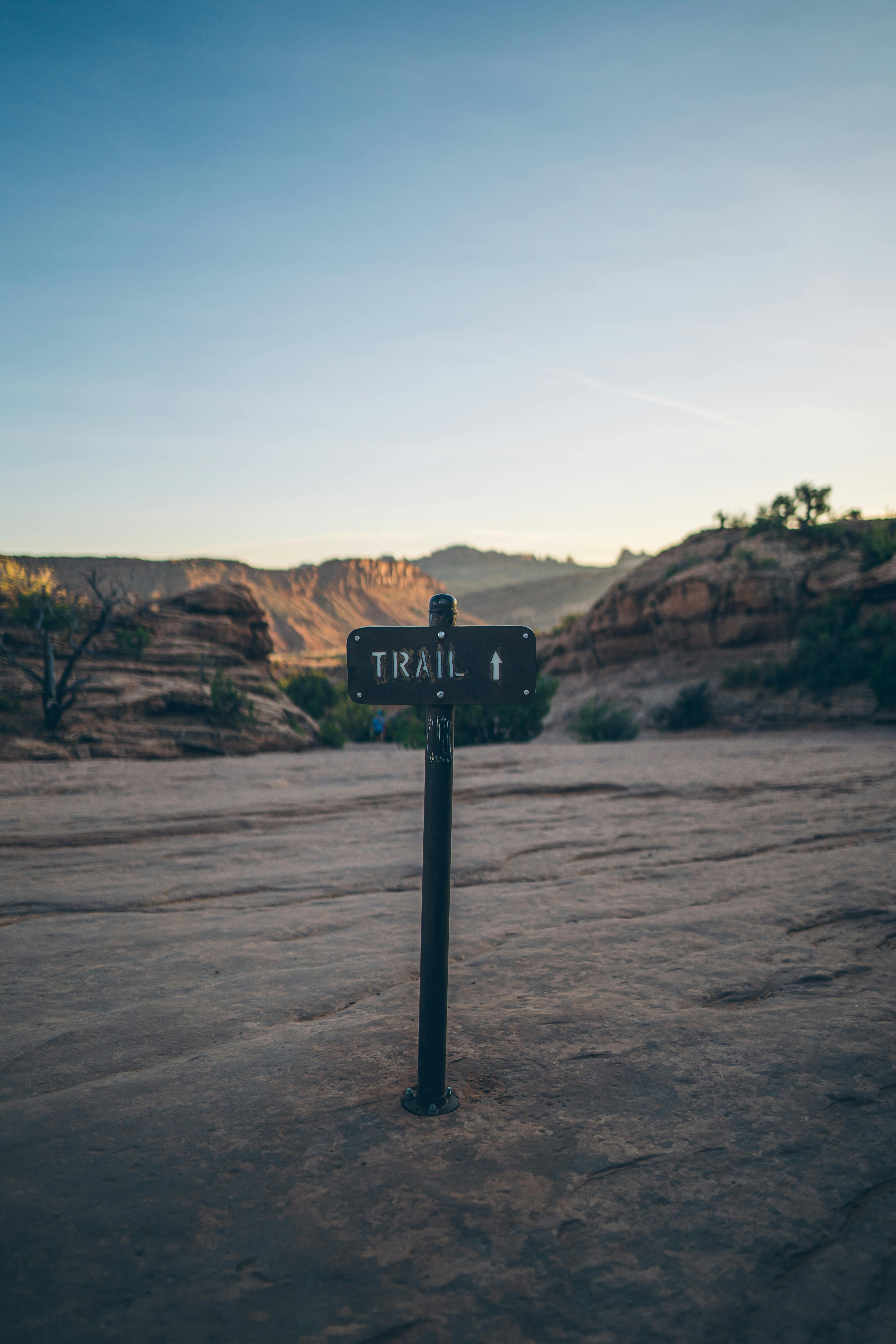 Signpost indicating a hiking trail in a desert landscape with rocky formations under a clear sky.