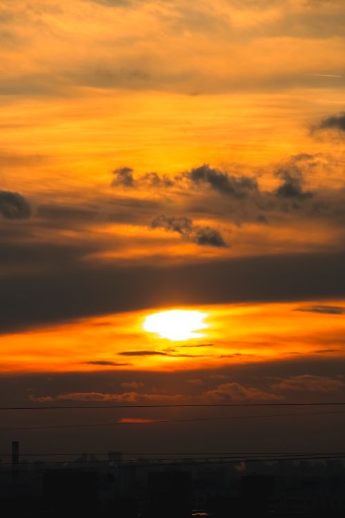 Free Stunning golden sunset with dramatic clouds creating a silhouette of the skyline below. Stock Photo