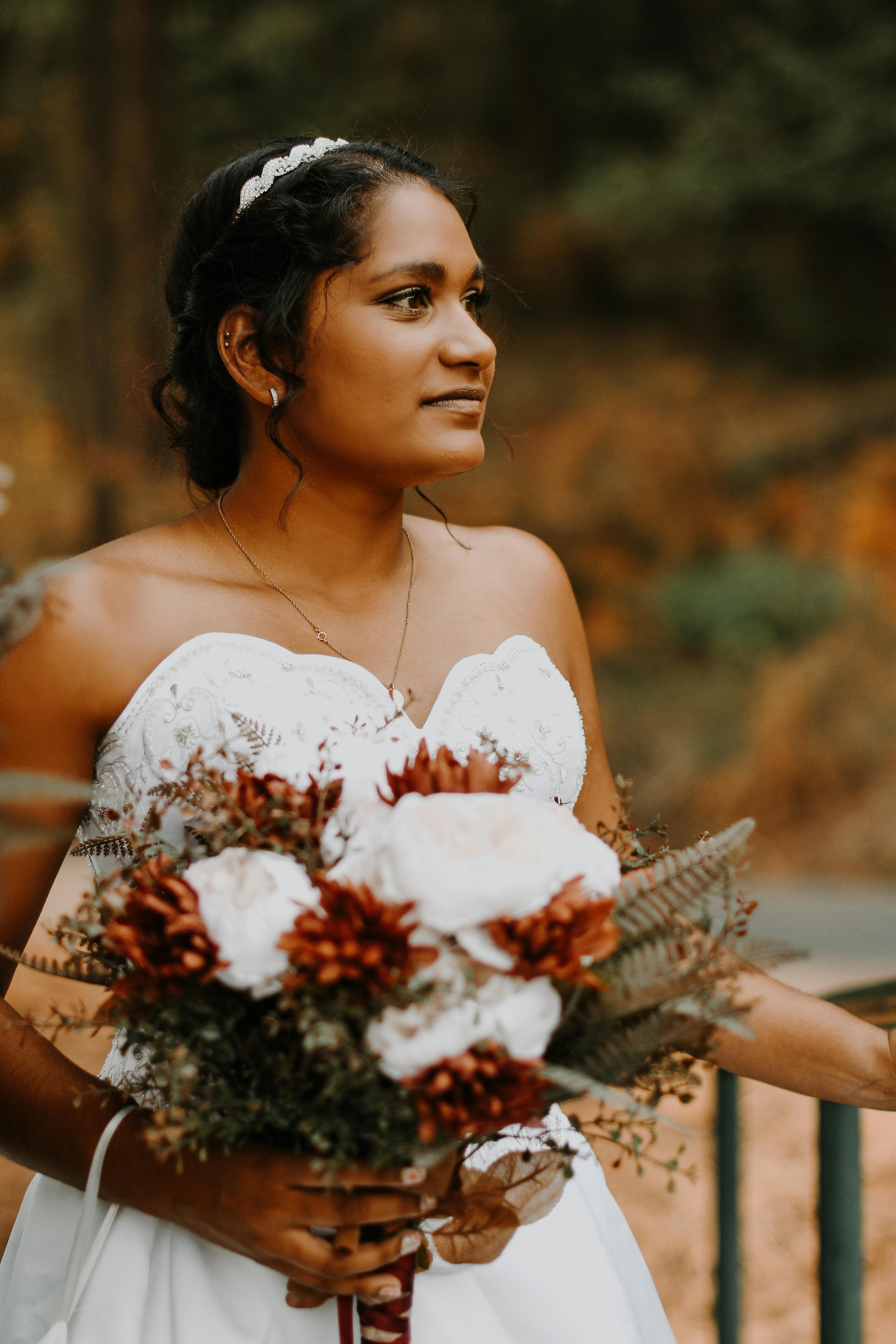 A beautiful bride holding a bouquet, gazing away with elegance in an outdoor autumn setting.