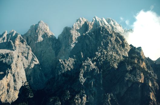 A stunning view of jagged rocky mountain peaks reaching high into a clear blue sky with scattered clouds.