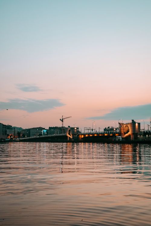 Free Beautiful sunset view of a city bridge reflecting on a calm body of water. Stock Photo