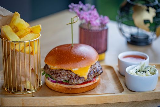 Delicious gourmet cheeseburger served with fries and dips on a wooden tray.