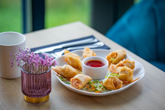Fried folded wontons on a white plate with carrot slaw and a cup of chili sauce