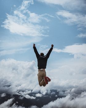 Man energetically leaps into the air amidst breathtaking mountainous backdrop and clear skies, exuding freedom.