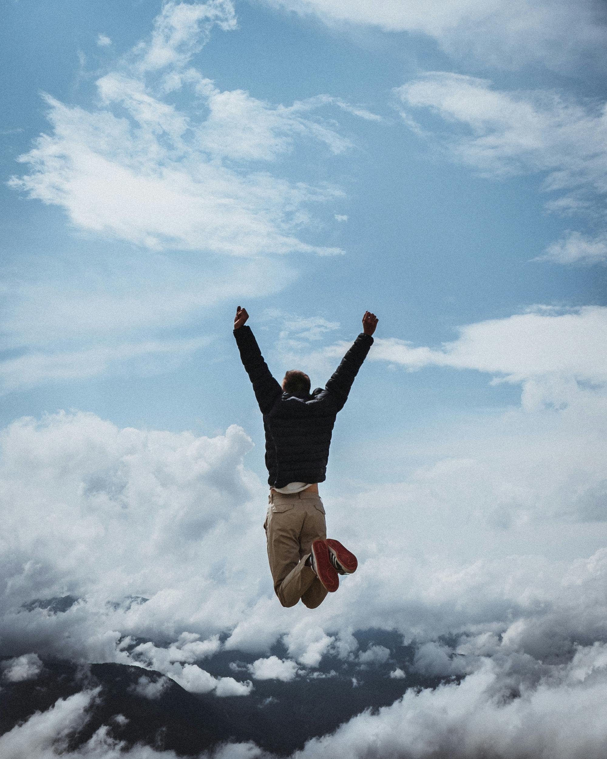 Person Jumping On Air With Clouds Background · Free Stock Photo