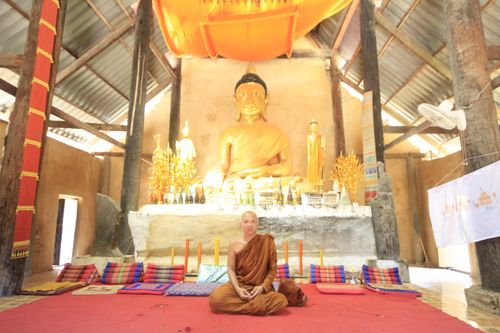 Free A monk meditates in a Buddhist temple with a large golden Buddha statue behind. Stock Photo