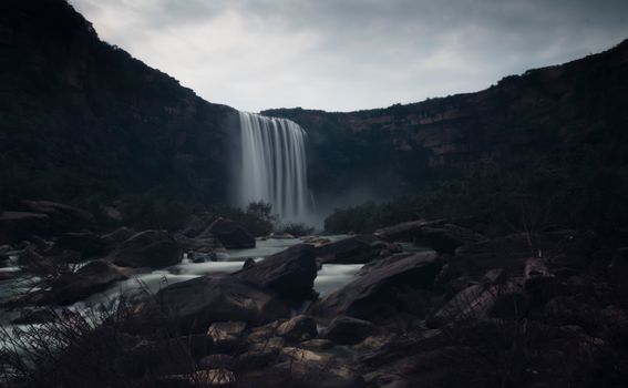 Stunning long exposure of a waterfall cascading into a rocky river under a cloudy sky.