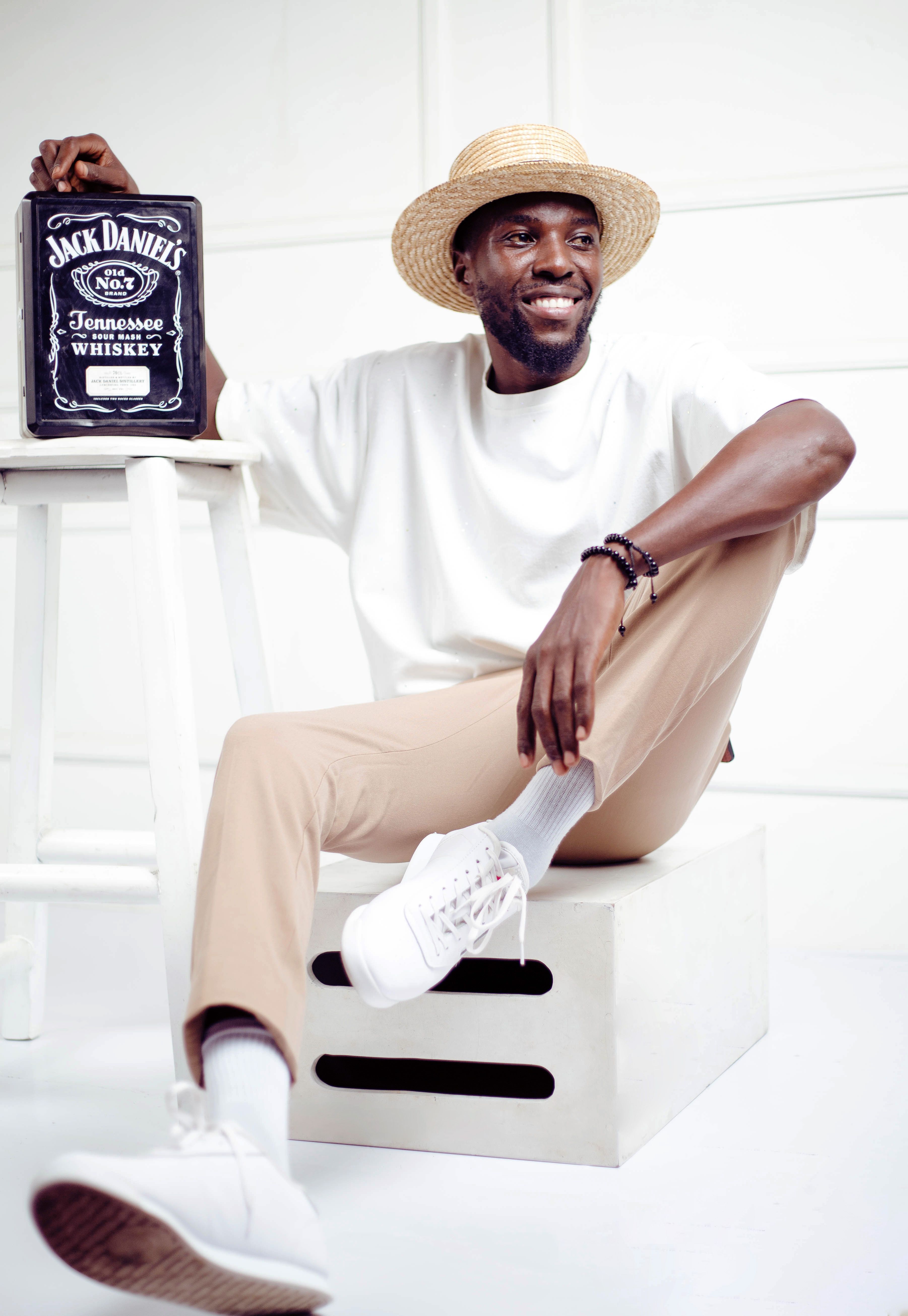 Man in straw hat sitting casually with a Jack Daniel's tin, smiling.