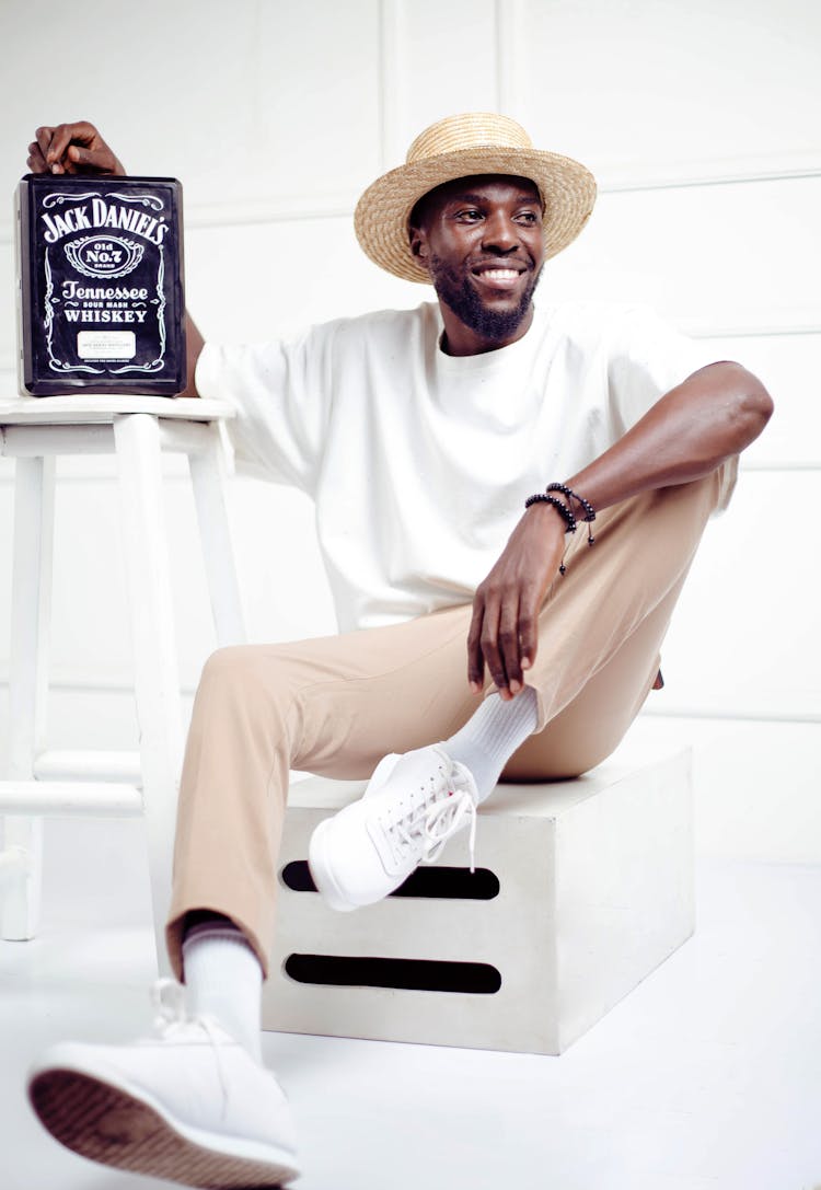 A Man Sitting On Crate Touching Jack Daniel Tin Box