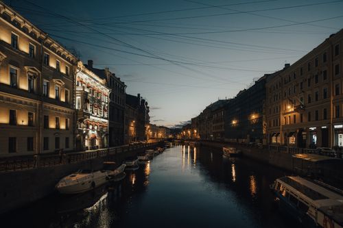 Free Illuminated canal in St. Petersburg at night with boats and reflections creating a serene urban atmosphere. Stock Photo