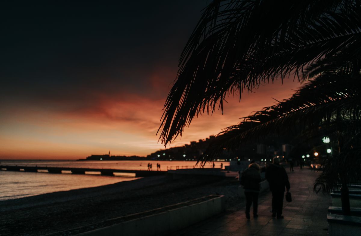 Figures walking along a palm lined promenade in Budva at dusk