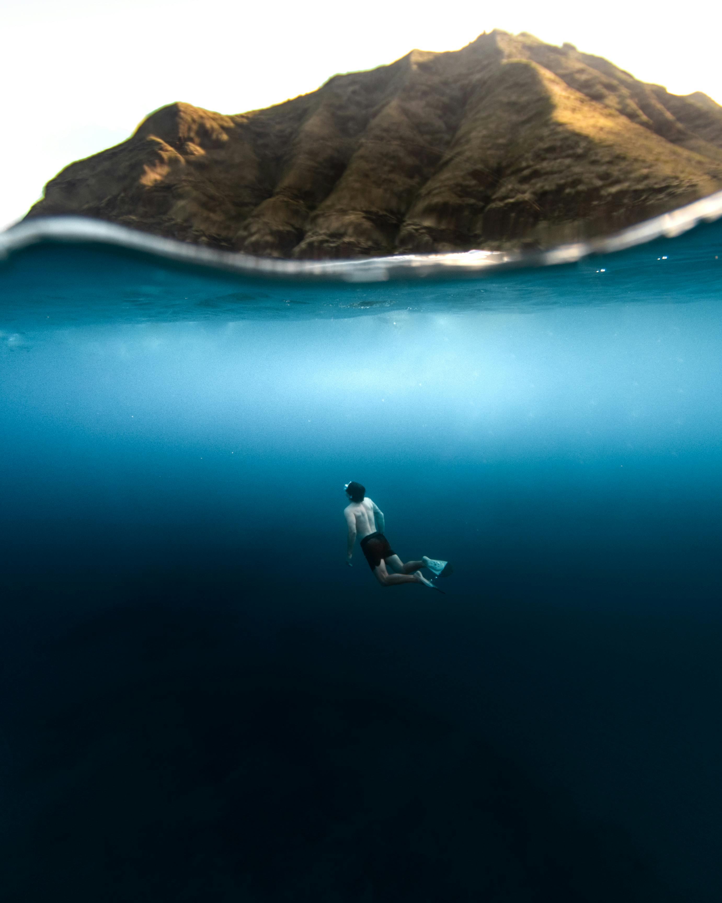 A snorkeler with diving flippers exploring underwater near a scenic rocky island.