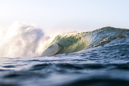 A powerful ocean wave curls and crashes under the gentle light of sunrise, showcasing nature's raw beauty.
