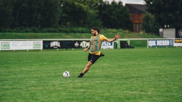 Athletic male soccer player executing a powerful kick on a lush green football field.