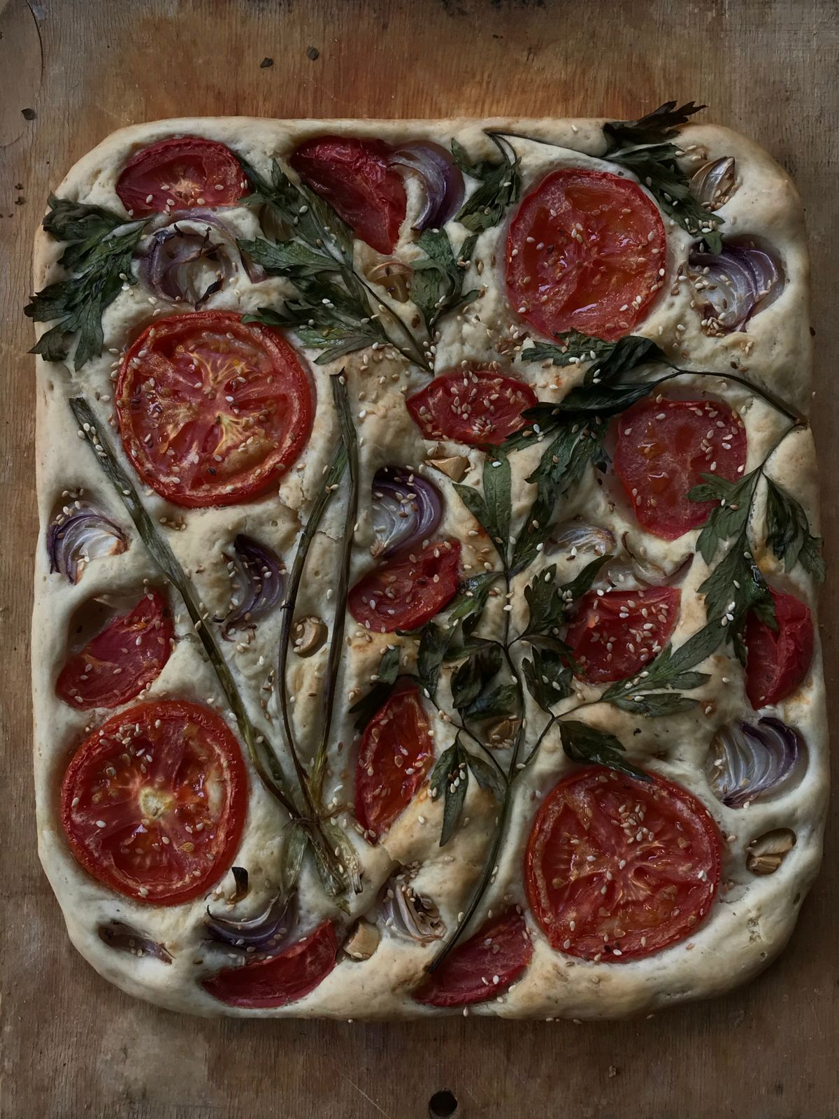 Focaccia topped with tomato slices, red onion and herbs, seen from above