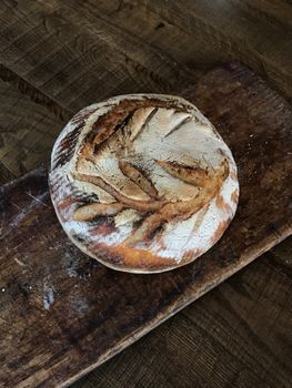 A freshly baked rustic sourdough bread loaf on a vintage wooden board, exuding a homey feel.