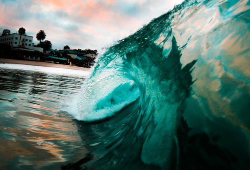 Free Vibrant ocean wave crashing near the shore, reflecting the colorful sky at sunset. Stock Photo