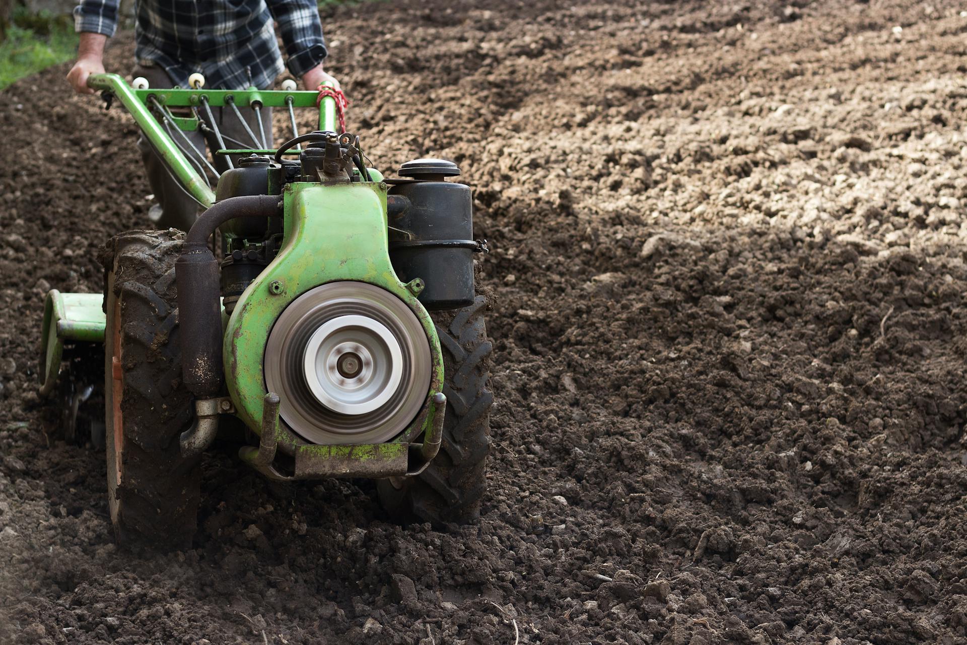 A farmer operates a walking tractor in a freshly plowed field, preparing the soil for planting.