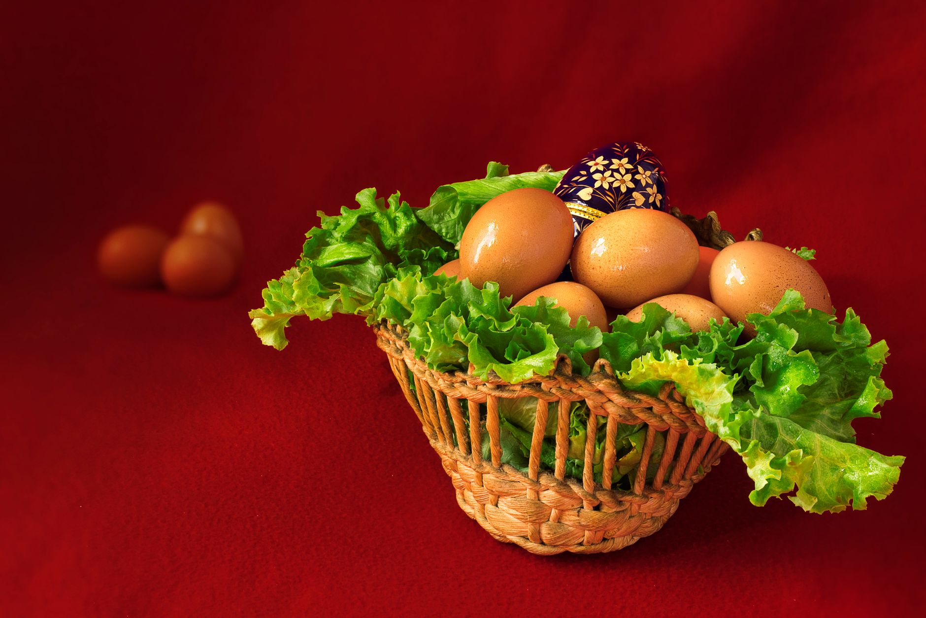 A basket of fresh eggs with lettuce leaves on a vibrant red background.