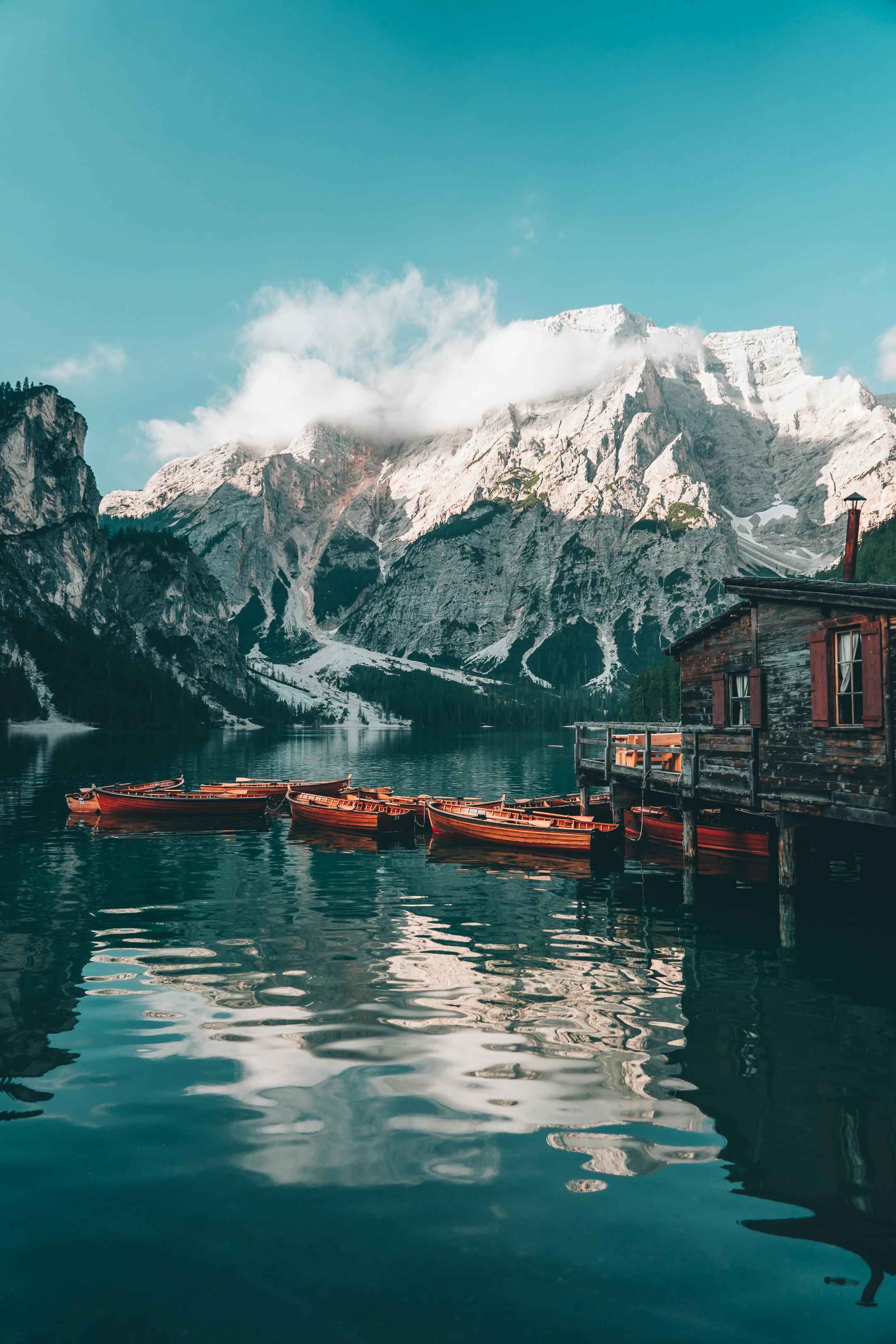 Tranquil scene of wooden boats floating on a lake against a backdrop of snow-capped mountains and blue sky.