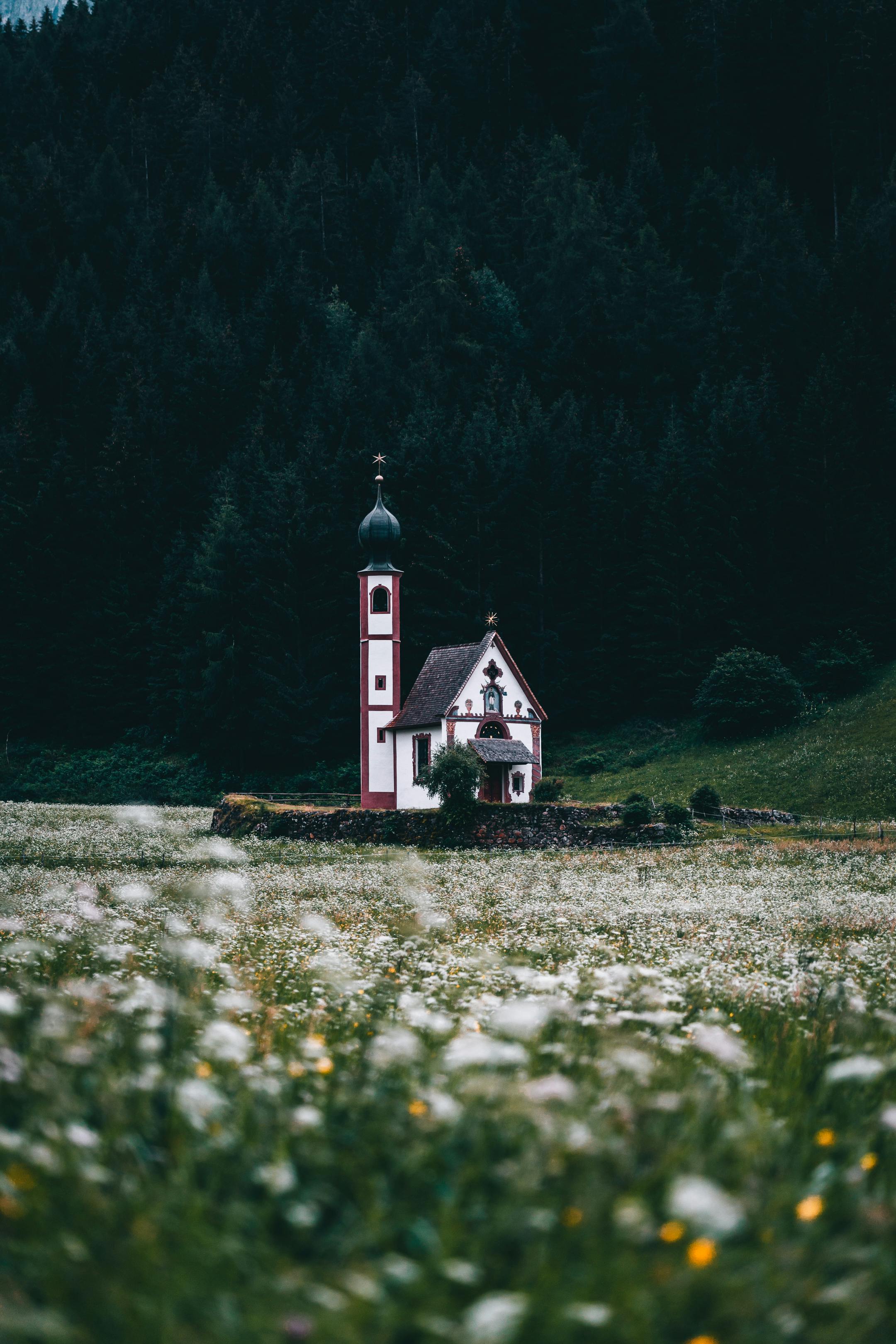 Picturesque scene of St. John Church in Italy, surrounded by lush meadows and forested hills.