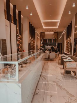 Cozy modern coffee shop interior featuring marble flooring and seating area with people.