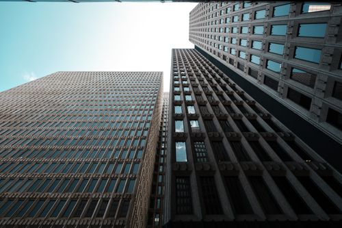 Free Low angle view of skyscrapers with glass windows reflecting a clear blue sky. Stock Photo