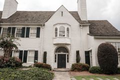 Elegant white brick house with green shutters, lush garden, and a curved walkway accentuating its classic facade.