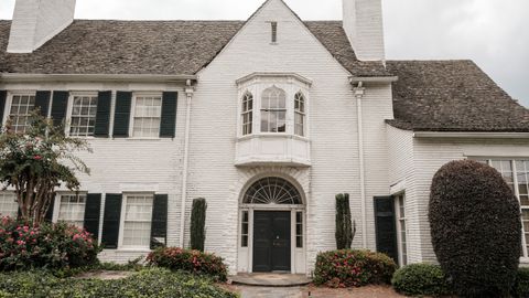 Elegant white brick house with green shutters, lush garden, and a curved walkway accentuating its classic facade.