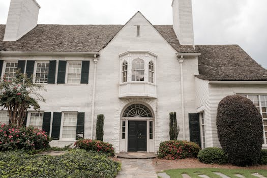 Elegant white brick house with green shutters, lush garden, and a curved walkway accentuating its classic facade.