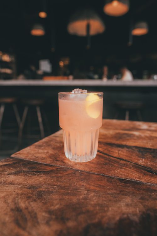 Free A chilled mocktail with lemon garnish sits elegantly on a rustic wooden table in a cozy indoor setting. Stock Photo