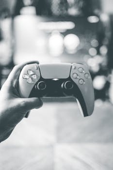 Black and white close-up of a hand holding a video game controller, emphasizing gaming technology.