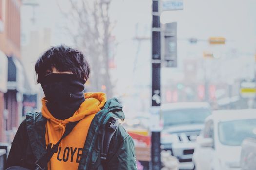 A person in a hooded jacket walks along a snowy urban street with cars.