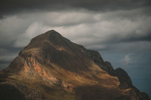 Free Explore a rugged mountain peak under a dramatic, cloudy sky, capturing nature's raw beauty. Stock Photo