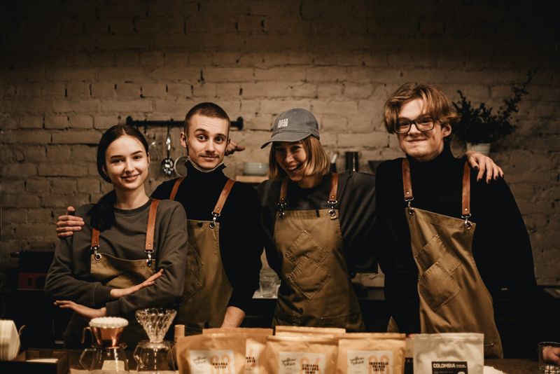 Four cheerful coffee shop staff in aprons standing together