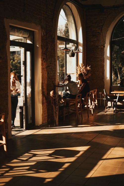 Free Warm sunlight streaming into a cozy coffee shop with people enjoying the relaxed atmosphere. Stock Photo