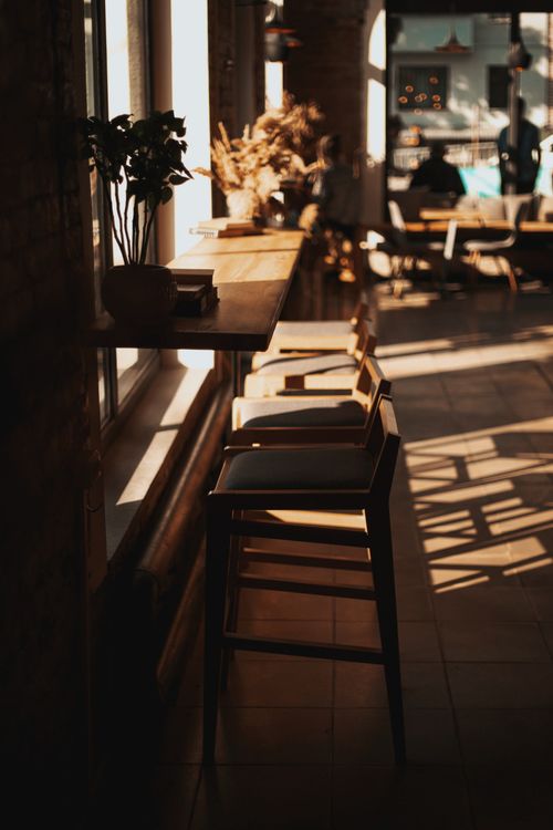 Free Cozy cafe interior featuring rustic chairs and warm sunlight streaming through large windows. Stock Photo