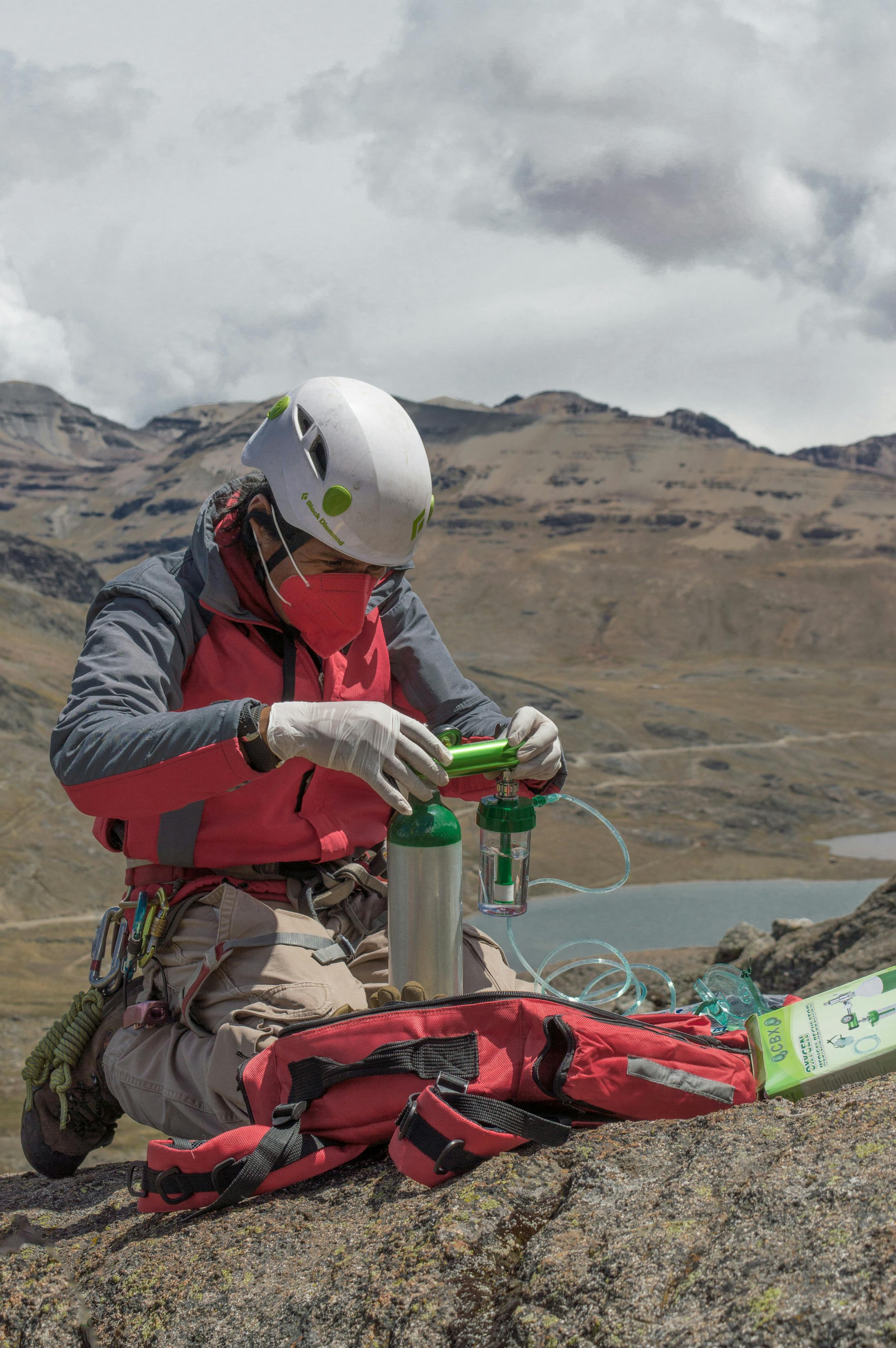 Climber sets up oxygen tank on a mountain, emphasizing safety in high-altitude climbing.