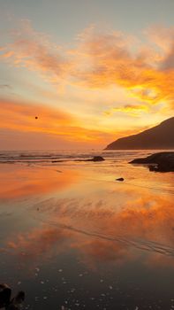Stunning sunset at a serene beach in Florianópolis, Brazil, with vibrant orange skies reflecting on calm waters.