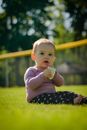 A Young Girl Sitting on the Grass while Eating a Biscuit