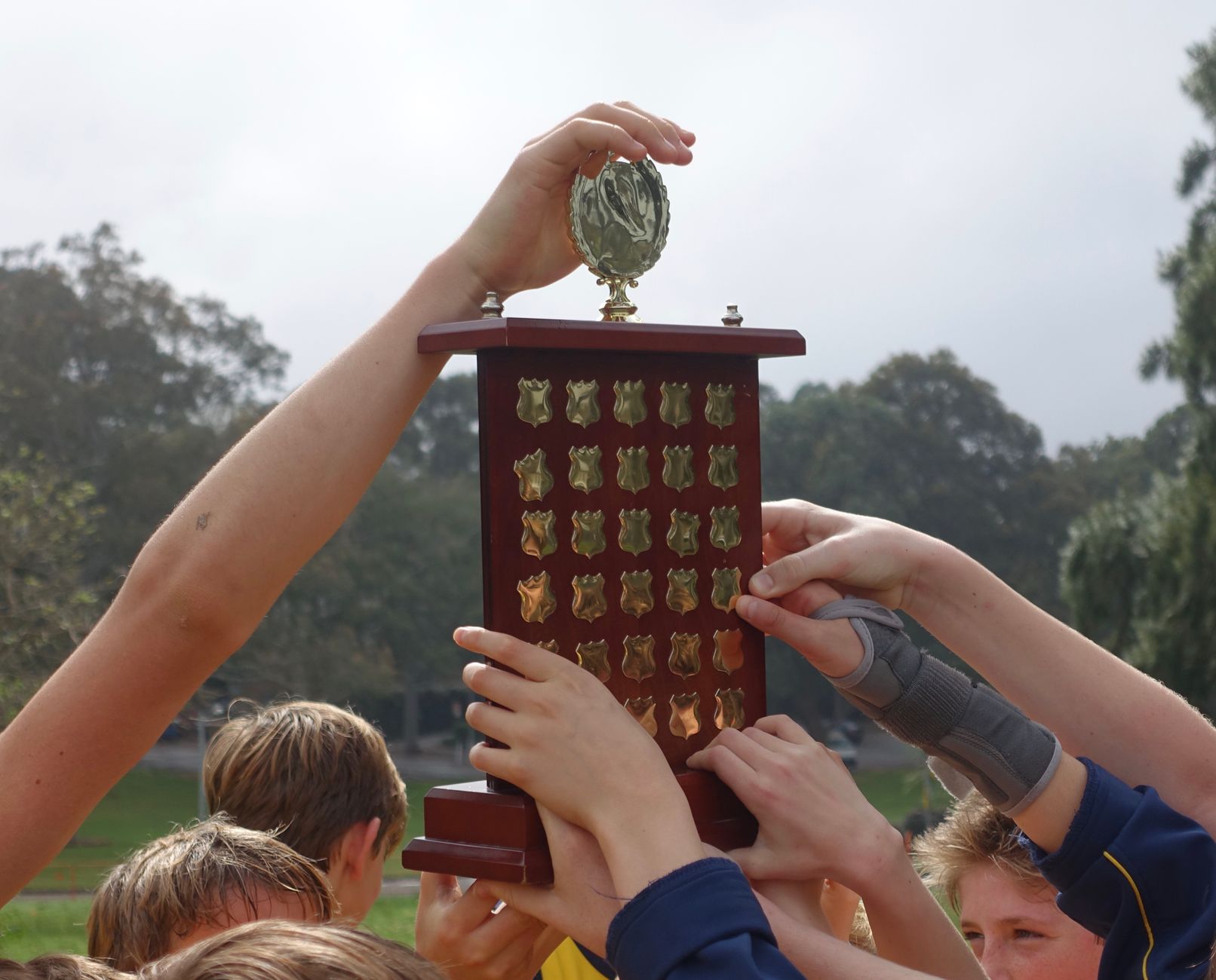 Group of young athletes raising a wooden trophy, symbolizing victory and teamwork.