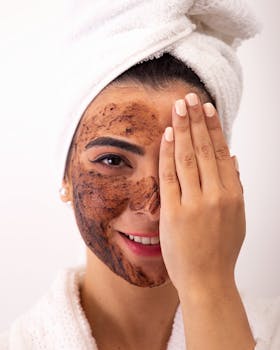 Close-up of a woman smiling and applying a facial mask in a bathrobe and towel.